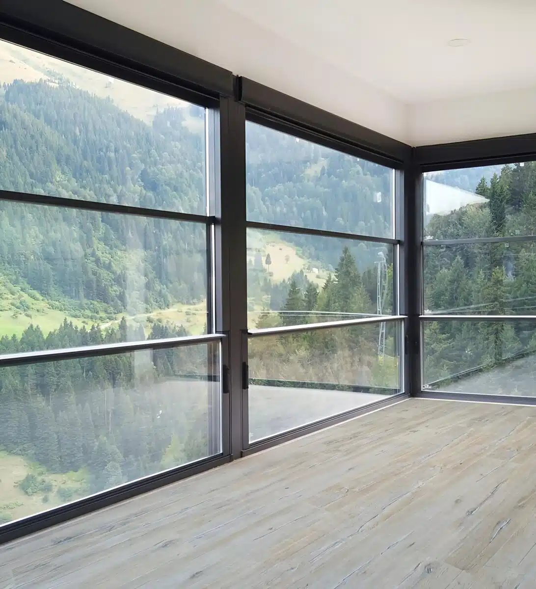 Modern black-framed vertical sliding windows in a bright interior, overlooking a scenic forested mountain landscape